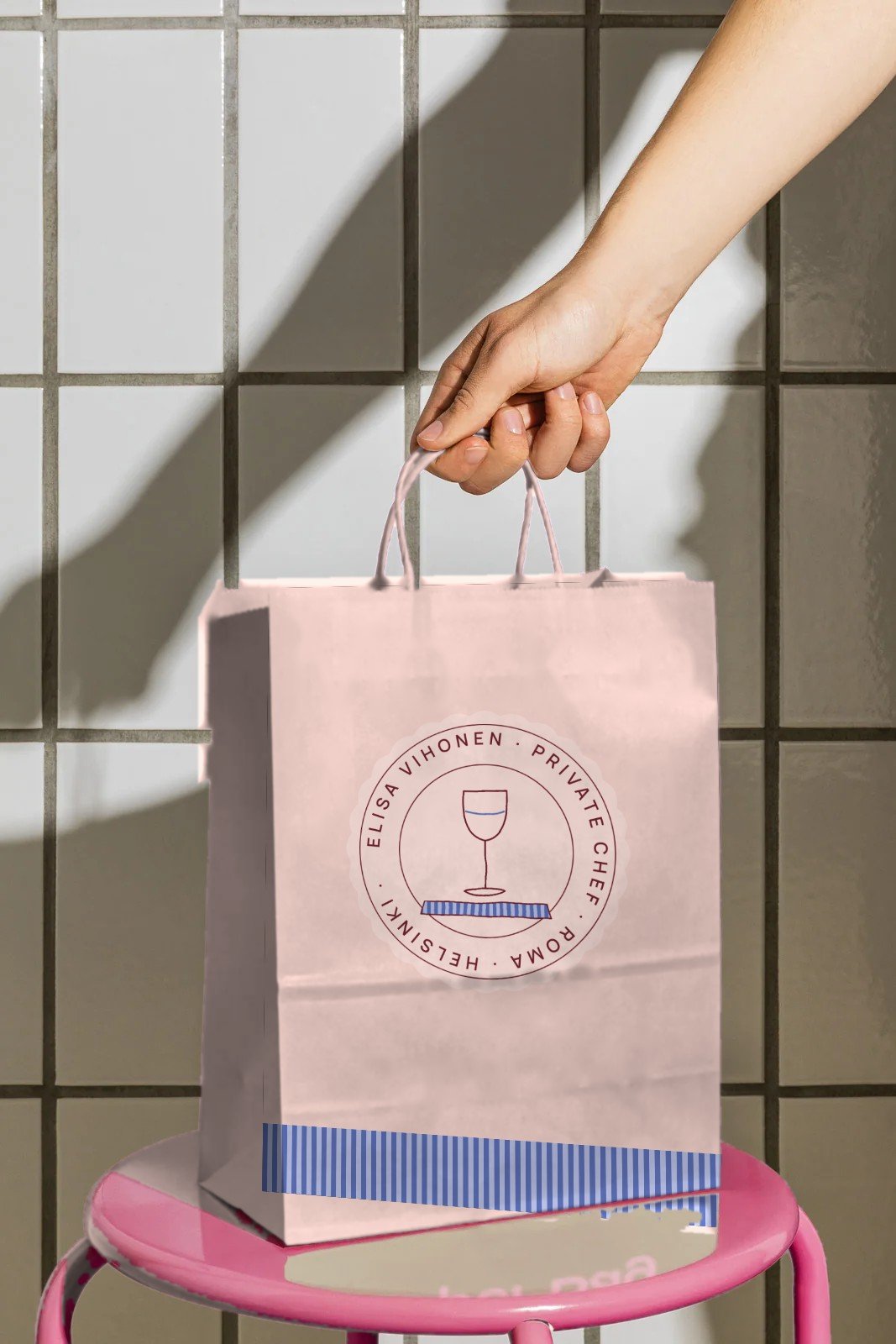 Pink takeaway bag with the Elisa Vihonen stamp, held in the sun